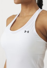 Weißes Sporttanktop mit strukturierter Oberfläche, dünnen Trägern und einem schwarzen Logo auf der linken Brustseite.
