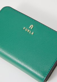 Grønn lærpung med teksturert overflate, gull "Furla"-logo og kontraststing. Kompakt rektangulær form med avrundede kanter.