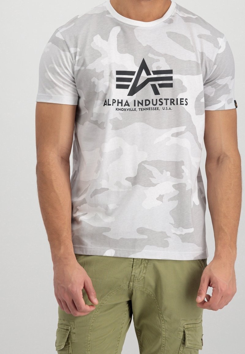 Biała koszulka w kamuflażu ma krótkie rękawy i okrągły dekolt. Czarne logo "ALPHA INDUSTRIES" nadrukowane na klatce piersiowej. Wykonana z miękkiego bawełnianego materiału.