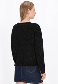 Zwarte gebreide trui met witte stipdetails, ronde halslijn en geribbelde manchetten. Draagt over een denim rok, van achteren gepresenteerd.