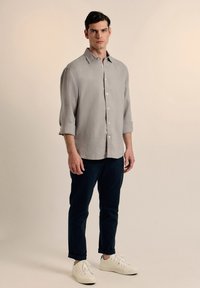 Camisa de lino gris con una textura sutil, abotonada en la parte delantera y con mangas dobladas, combinada con pantalones azul marino y zapatillas blancas.