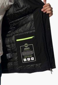 Giacca termica nera con fodera interna trapuntata. Presenta una tasca con zip verde neon e un'etichetta per la cura dei tessuti cucita all'interno.