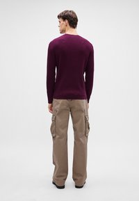 Bordeauxroter Strickpullover mit langen Ärmeln und Rundhalsausschnitt, kombiniert mit khakifarbenen Cargo-Hosen, die seitliche Taschen und eine lässige Passform aufweisen.