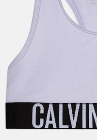 Világoslila, varrás nélküli sportmelltartó, puha anyagból, széles fekete elasztikus pánttal, amelyen fehér "CALVIN" logó található.