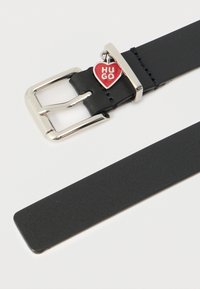 Mustast nahast vöö, millel on hõbedane metallpandlaga ja punane südamekujuline ripats, millel on tekst "HUGO". Sile tekstuur väheste kaunistustega.