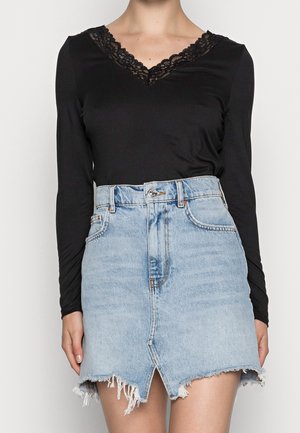 Femme portant un haut noir à manches longues avec un col en V en dentelle et une mini-jupe en jean bleu clair délavé avec une fente à l'avant et un ourlet effiloché.