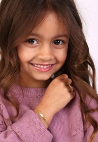 Gouden sieraden, waaronder een armband met een glad, vlak oppervlak en een decoratieve ring, gedragen door een kind in een lichtpaarse gebreide trui.