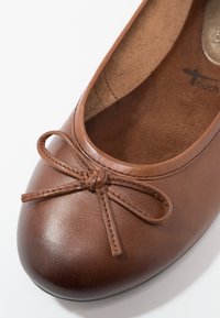 Ballerine en cuir marron avec un nœud cousu sur l'avant arrondi et une semelle intérieure douce et rembourrée.