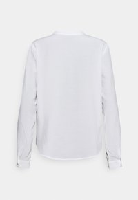 Chemise blanche à manches longues avec une texture douce, un col arrondi et des poignets à boutons, présentant un design simple au dos et sans motifs visibles.