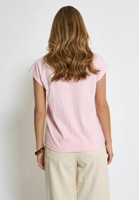 Šviesiai rožinė trumpomis rankovėmis marškinėliai su laisvu siluetu ir sulankstytomis rankovėmis, pagaminti iš minkštos medvilnės. Lygus paviršius, šiek tiek išlenktas apatinis kraštas.