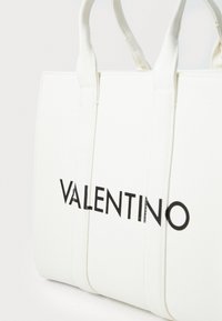 Biała torba tote z płótna z czarnym logo "VALENTINO". Posiada usztywniony kształt oraz mocne, podwójne uchwyty. Gładka faktura, minimalistyczny design.