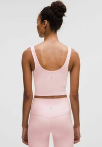 Roza sportska crop majica s izrezom na leđima, u kompletu s visokim tajicama. Glatka, rastezljiva tkanina s minimalnim brandingom.