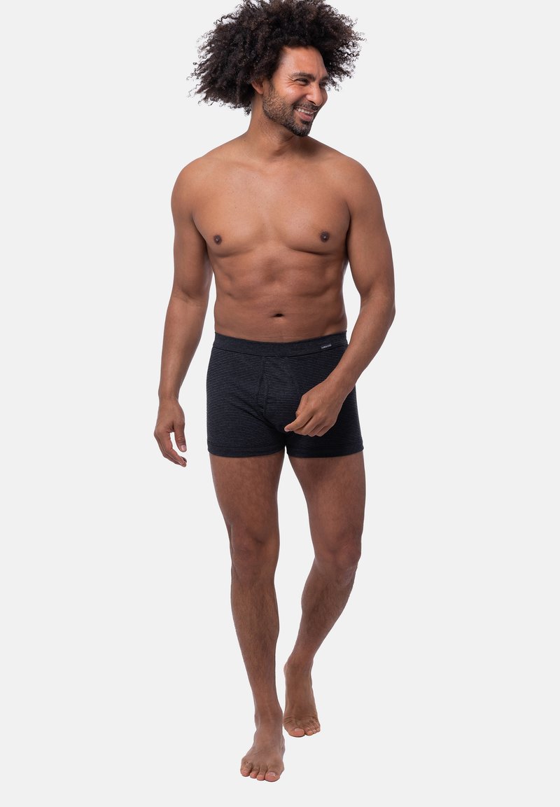 Boxer shorts a righe nere realizzati in tessuto morbido, con vita elastica e vestibilità aderente, modello in posa in piedi a piedi nudi.