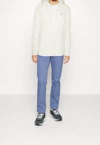 Ljusgrå hoodie med dragsnören, blå byxor och svarta sneakers. Hoodien har en logotyp; byxorna har en rak passform. Strukturerad tyg overall.