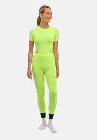 Jasnozielony, dopasowany strój sportowy z krótkimi rękawami, bezszwowy i z czarnymi akcentami. Noszony z białymi skarpetkami.