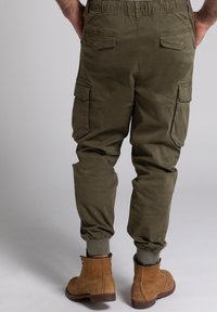 Grüne Cargo-Hose mit einem elastischen Bund, Knöchellöchern, mehreren Seitentaschen und einer glatten Textur. Getragen mit braunen Stiefeletten.