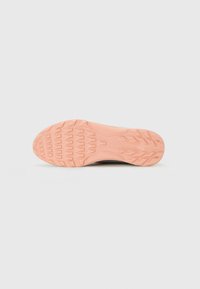 Lyserød gummisål på en sneaker med teksturerede grebsmønstre på en ensfarvet hvid baggrund.