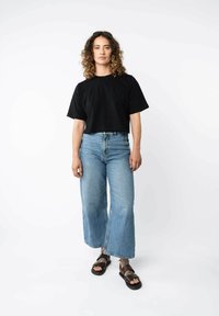 Zwart cropped t-shirt, lichtblauwe wijde jeans, bruine sandalen met verstelbare banden, versleten denim textuur, minimalistisch design.