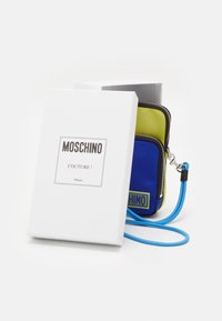 Borsa Moschino blu e verde brillante con chiusura a zip, caratterizzata da un design alla moda e una tracolla blu, presentata in una scatola bianca con logo.