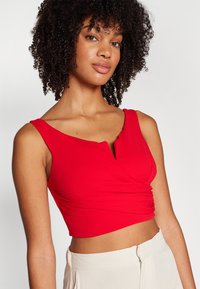Crop top rosso con scollatura a V, dettagli arricciati sul davanti e spalline larghe, realizzato in un tessuto elastico e morbido.