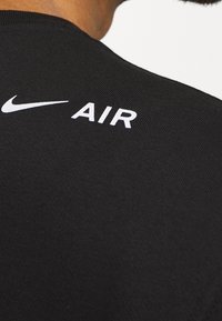 Musta kangas, jossa on poimutettu rakenne; valkoinen "Nike"-logo ja "AIR"-teksti takana, lähellä kaulusta.