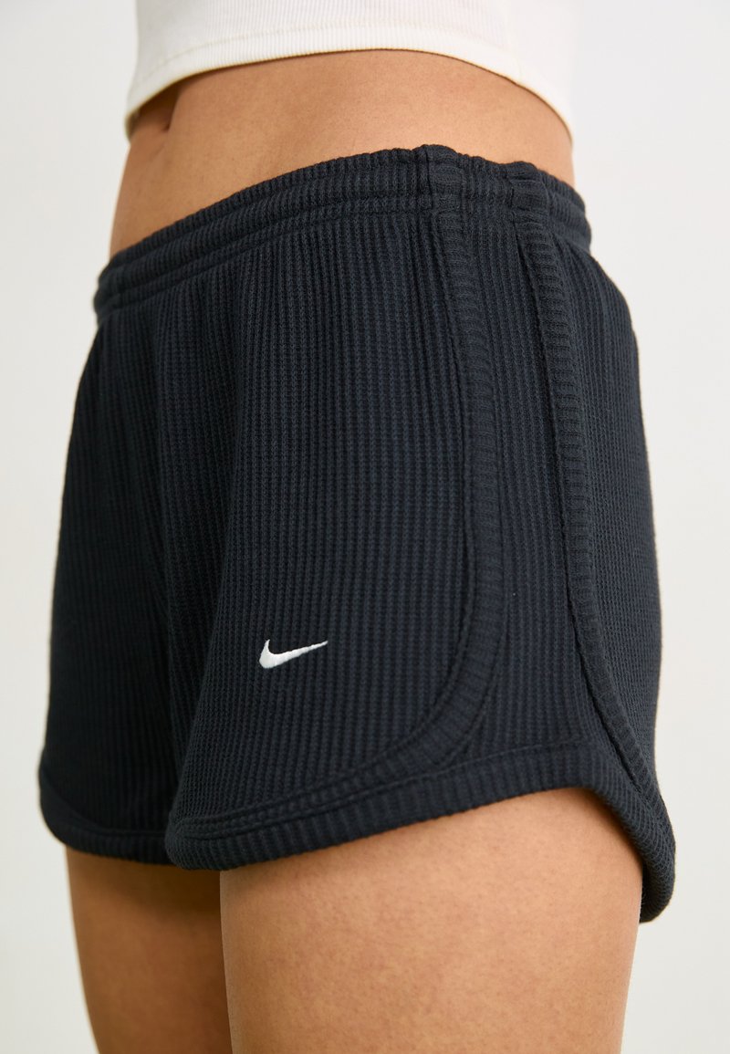 Schwarze gerippte Shorts mit elastischem Bund, ausgestattet mit einem weißen Nike-Logo und einem seitlichen Saumdesign für zusätzliche Details.