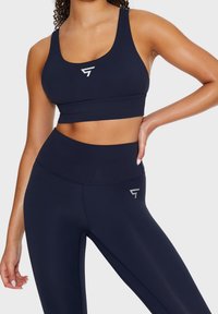Marinblå sportig crop top och högmidjade leggings gjorda av elastisk, fukttransporterande tyg; har en silverlogga på varje plagg.