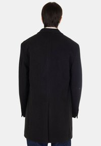 Cappotto di lana nero con vestibilità su misura, presenta rever a taglio, spacco singolo e maniche lunghe. La vista posteriore mostra un design pulito e una texture liscia.