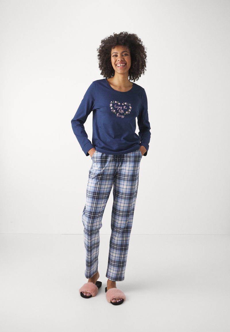 Marinblå långärmad skjorta med blommönster och text, ihop med rutiga pyjamasbyxor i blå toner. Ljust rosa fluffiga tofflor fulländar looken.