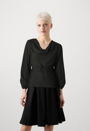 Blusa nera con collo a cowl e maniche lunghe a sbuffo, abbinata a una gonna nera svasata. Tessuto morbido e fluido.