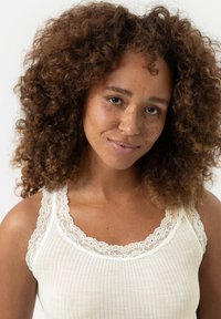 Witte geribde tanktop met ingewikkelde kantafwerking langs de halslijn en schouderbanden, met een zachte textuur en een aansluitend ontwerp.