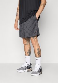 Grå idrettsshorts med et geometrisk mønster, brukt med svart og hvitt sneakers og hvite sokker. Har lommer og en avslappet passform.