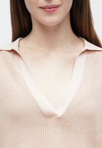 Pull rose clair en maille avec un col en V et un col contrasté. La texture est respirante avec un design tissé lâche et ouvert.