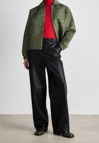 Zielona pikowana kurtka bomber, czerwona golf, czarne szerokie spodnie z sztucznej skóry i ciemnozielone buty. Gładka tekstura i sportowy krój.