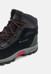 Czarne buty trekkingowe z górną częścią wykonaną z zamszu i siateczki, czerwone i czarne sznurówki, szara podeszwa środkowa oraz teksturowana podeszwa z gumy. Widoczne logo marki Columbia.