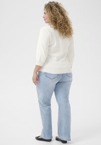 Light cream pullover sweater with three-quarter sleeves, paired with light blue denim jeans and black flats. Soft texture and relaxed fit.