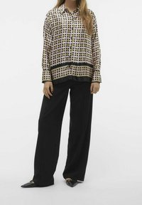Blusa a quadri intrecciati in colori chiari con bordo nero, abbinata a pantaloni neri larghi; modella che indossa mocassini neri a punta.