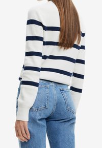 Pull rayé blanc à rayures horizontales bleu marine, avec poignets et col côtelés, associé à un jean denim bleu taille haute avec poches arrière.