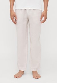 Pantalones de lino de color beige claro con un corte holgado, piernas rectas y aberturas laterales en el dobladillo, combinados con una camiseta blanca lisa.