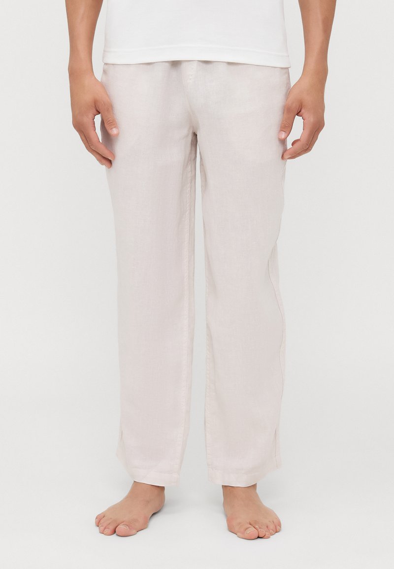 Pantalones de lino de color beige claro con un corte holgado, piernas rectas y aberturas laterales en el dobladillo, combinados con una camiseta blanca lisa.