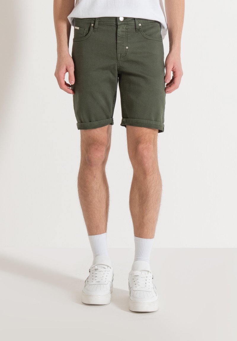 Olijfgroene denimshorts met omgeslagen zomen, met een klassieke vijf-pocket ontwerp en zilveren knopen, gedragen met witte sneakers.