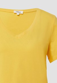 Gelbes V-Ausschnitt-T-Shirt aus weichem Stoff. Kurze Ärmel mit glatter Textur und leichtem Fall. Etikett sichtbar am Halsauschnitt.