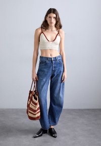 Krochetkowy jasnożółty biustonosz z czerwonym wykończeniem, dżinsy o wysokim stanie w kolorze niebieskim, czarne czółenka w szpic z ozdobami oraz paskowana torebka typu bucket.