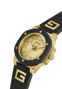 Goldfarbige Uhr mit rundem Zifferblatt, schwarzem Silikonarmband, auffälligen Ziffernmarkierungen und einer strukturierten Lünette mit goldenen Akzenten.