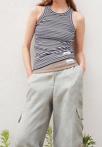 Top con righe in bianco e nero, con una texture a costine. Abbinato a pantaloni cargo grigi chiari, morbidi e larghi, dotati di tasche laterali.