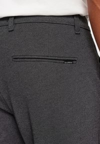 Pantalones grises con un sutil patrón de espiga, que cuentan con un bolsillo trasero, pasadores para cinturón y una pequeña etiqueta de la marca. Tejido texturizado.