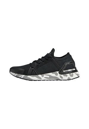 Zapatilla deportiva negra con parte superior de punto, cordones negros y suela blanca con patrones abstractos en negro y gris, vista de lado.