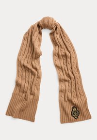 Sciarpa a maglia con trecce in una calda tonalità beige, caratterizzata da un design testurizzato e un patch con logo e dettagli dorati su un'estremità.