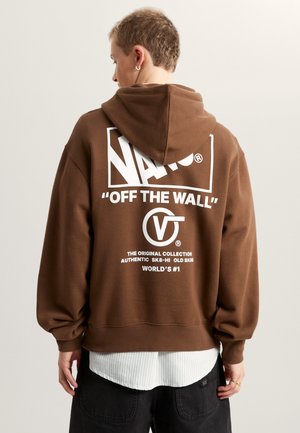 Brązowy hoodie z białym logo i tekstem na plecach. Posiada sznurki w kapturze i opadające ramiona, noszony na paskowaną koszulę.