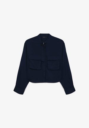 Marineblaue, kurz geschnittene Bluse mit langen Ärmeln, zwei Brusttaschen und einer Bindeschließe mit einem metallischen Ring-Accessoire. Glatte Stoffoberfläche.